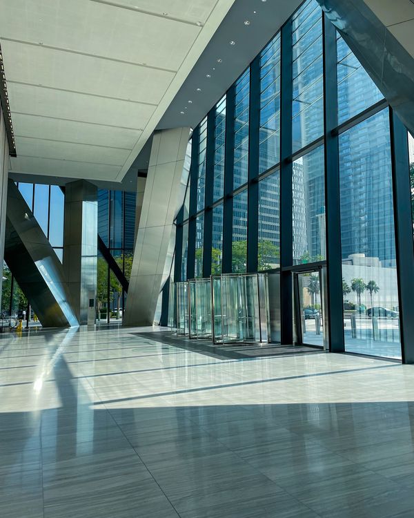 Helle Eingangshalle eines Bürogebäudes mit hoher Glasfront und spiegelndem Steinboden