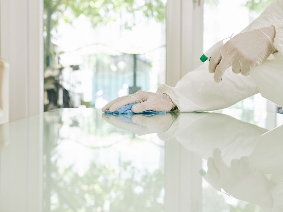 Hände in weißen Handschuhen wischen mit einem blauen Tuch eine Glasfläche
